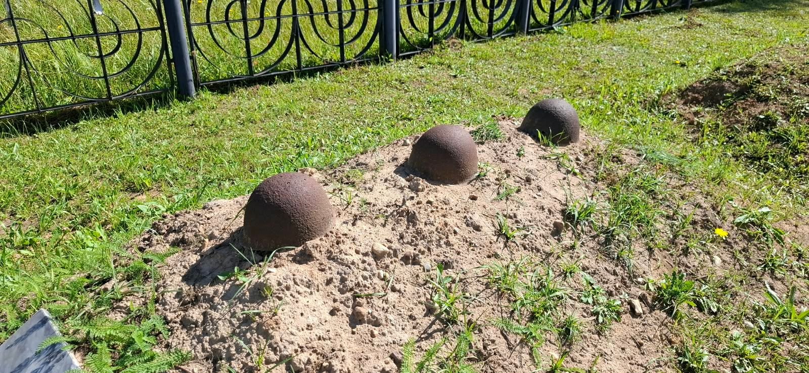 Cumuli di terra con elmetti sovietici sulle tombe dei caduti al memoriale di Barsuki, vicino a Juchnov